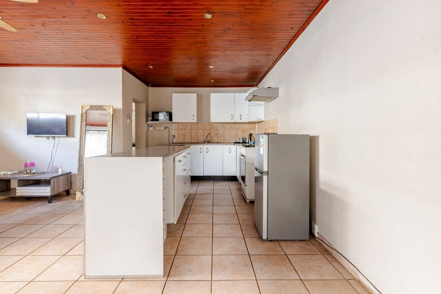 Eine moderne Küche mit weißen Schränken, einem grauen Kühlschrank und einer Holzbalkendecke.