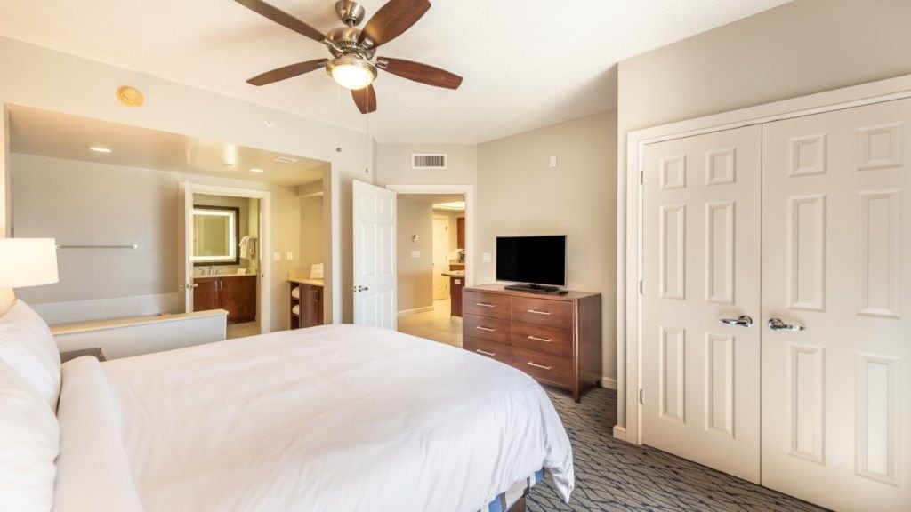 Ein Hotelzimmer mit Bett, Deckenventilator, Fernseher, Kommode und Kleiderschrank.