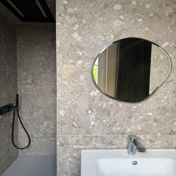 A bathroom with a white sink, a round mirror, and a shower area. - New Listing (cognac)