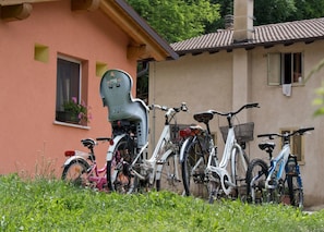 Flere cykler står parkeret foran en bygning med tegltag og et vindue med blomster.