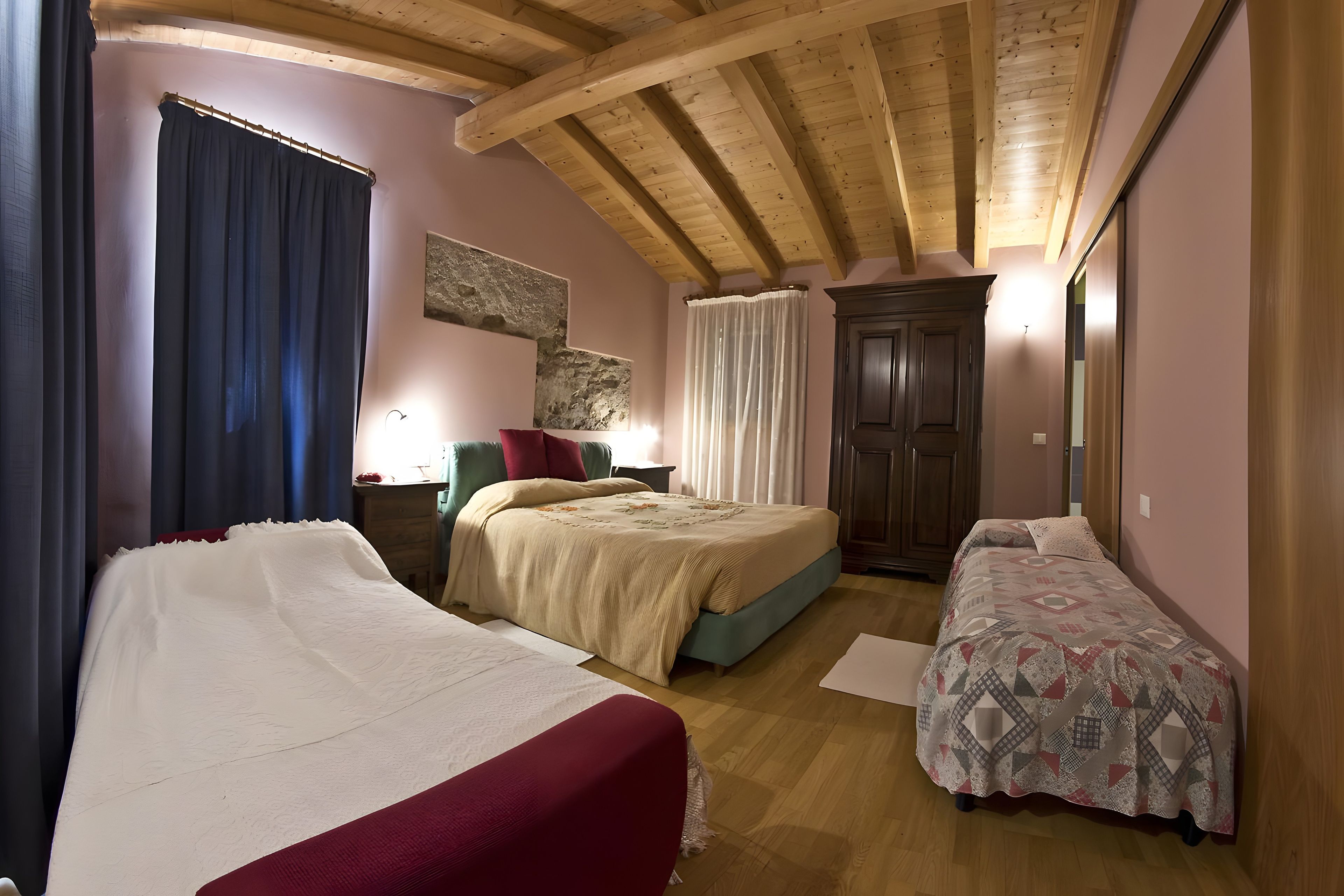 A room with two beds, a wooden ceiling, a door, and a wall with a textured surface.