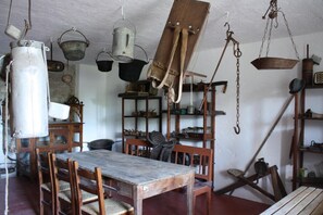 Una habitación rústica con una mesa de madera, sillas y varios utensilios de cocina colgando.