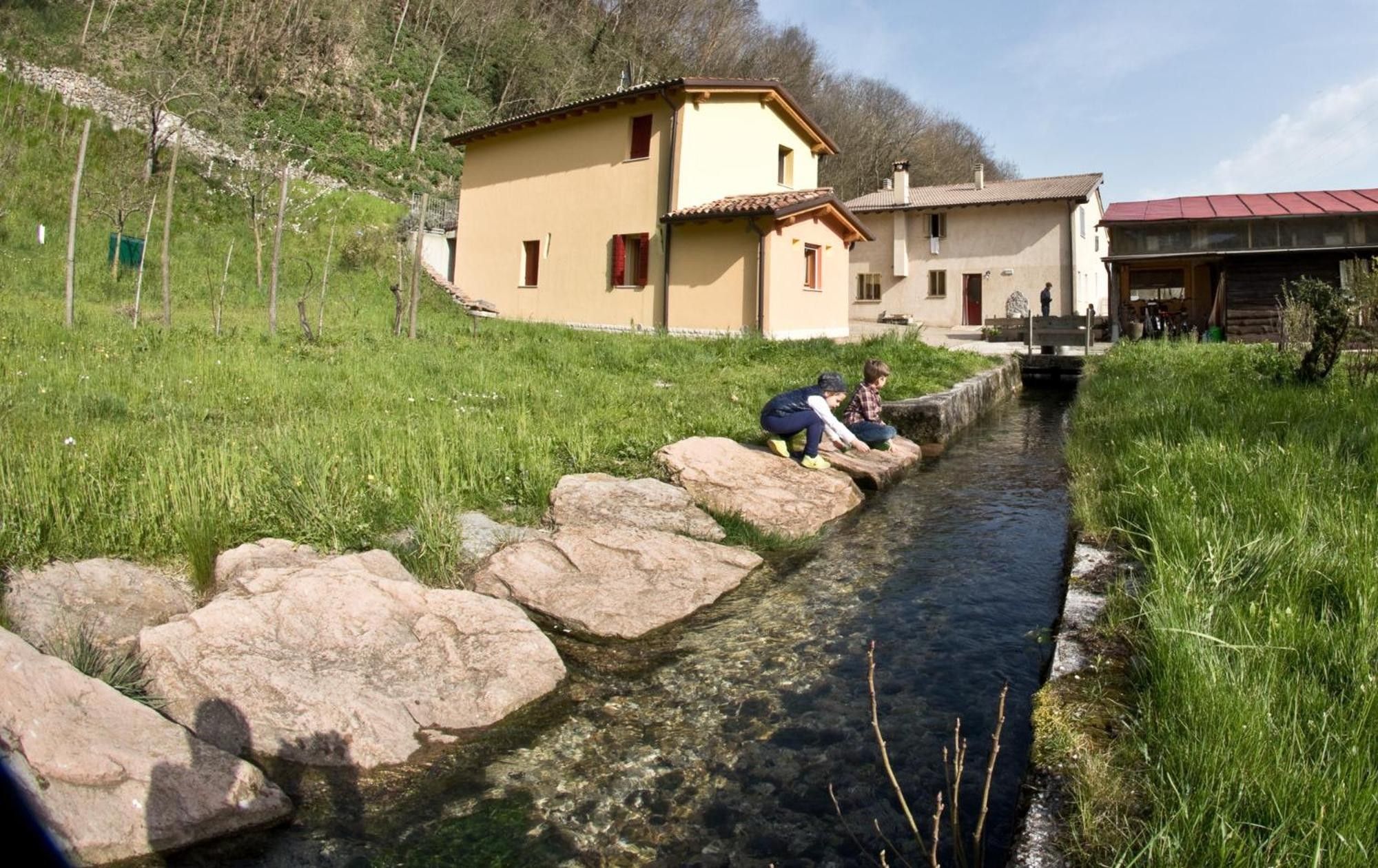 A narrow water channel with large rocks, a grassy area, and a building with a red roof.