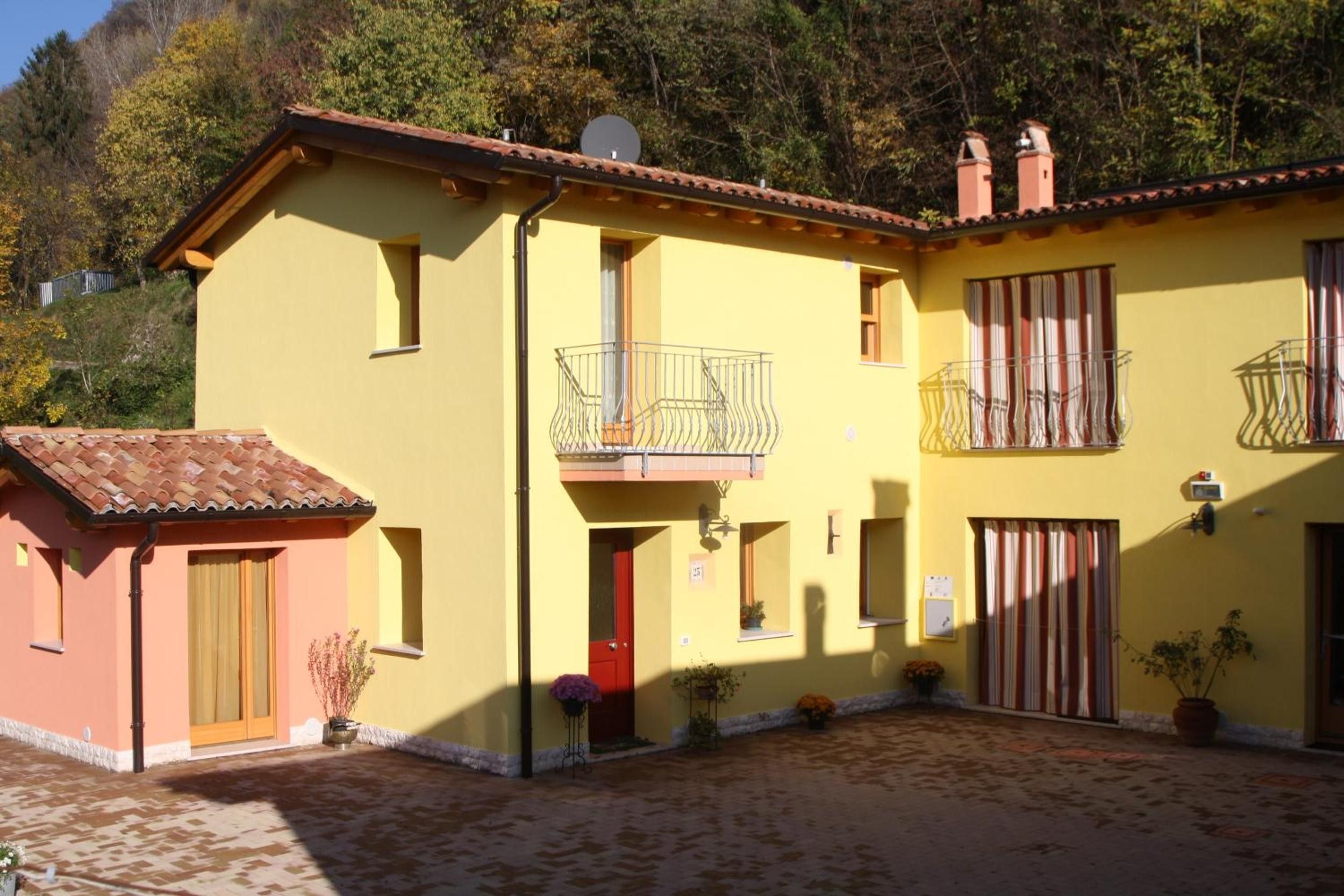 Un bâtiment jaune à deux étages, avec un toit recouvert de tuiles, un balcon doté d’une balustrade en métal et une porte rouge.