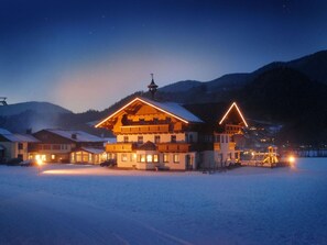 Ein schneebedecktes Gebäude mit mehreren Balkonen und einem beleuchteten Dach, umgeben von verschneiter Landschaft und Bergen.