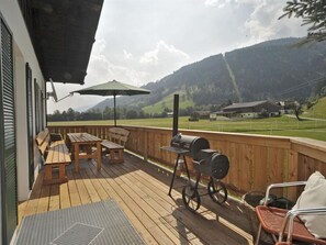 Eine Holzterrasse mit Gartenmöbeln, einem Grill und Blick auf eine Berglandschaft.