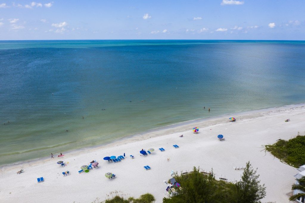 A beach with clear turquoise water, white sand, and several beach umbrellas and lounge chairs.