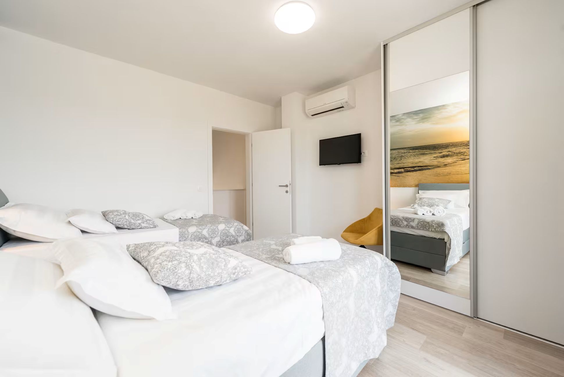A modern bedroom with a bed, a TV, and a large mirror reflecting a sunset view.