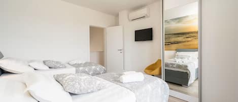 A modern bedroom with a bed, a TV, and a large mirror reflecting a sunset view.