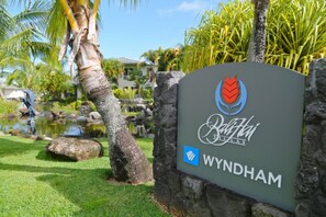 Letrero de Wyndham Bali Villas con logotipo, rodeado por un jardín tropical con palmeras y un estanque.