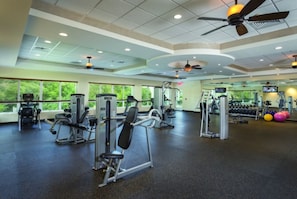 Un gimnasio con ventiladores de techo, equipo de ejercicio y ventanas amplias.