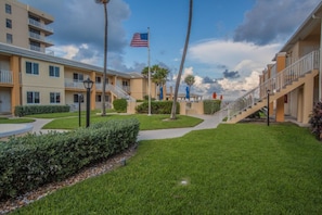 A hotel with multiple-story buildings, a flag, and a well-maintained lawn. - Gulfstream | Sunrise Beach Days | Pool + Beach (Gulfstream)