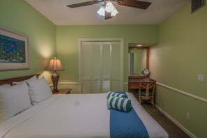 Ein Hotelzimmer mit Bett, Schreibtisch mit Stuhl, Lampe, Deckenventilator und einer Tür mit Fensterläden.