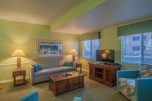 Ein Wohnzimmer mit einer Couch, einem Couchtisch, einer TV-Konsole und einem Fenster mit Jalousien.