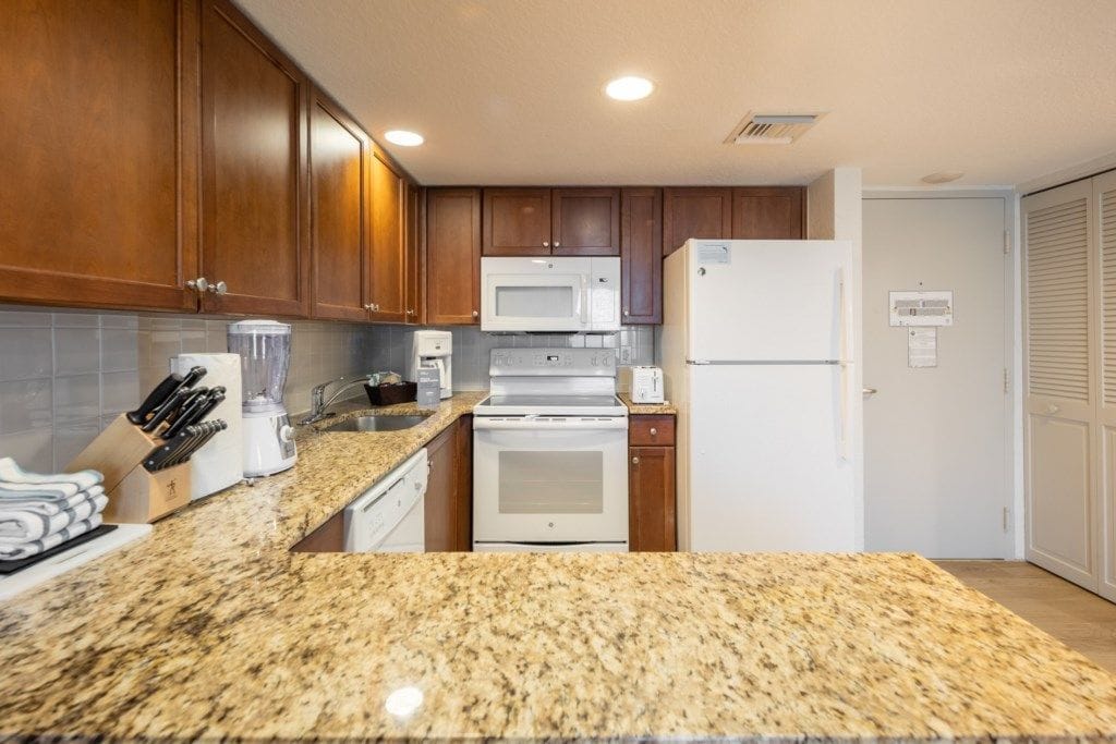 A kitchen with granite countertops, wooden cabinets, a white stove, a microwave, and a refrigerator.