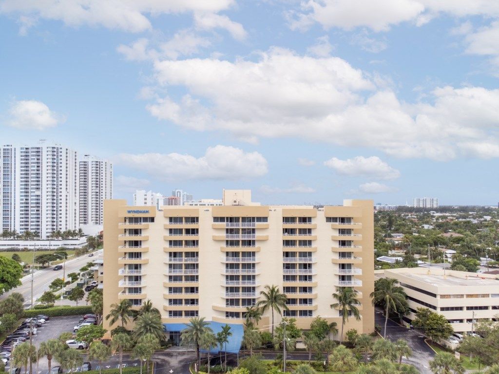 A multi-story hotel with a central courtyard, surrounded by palm trees and a parking lot.