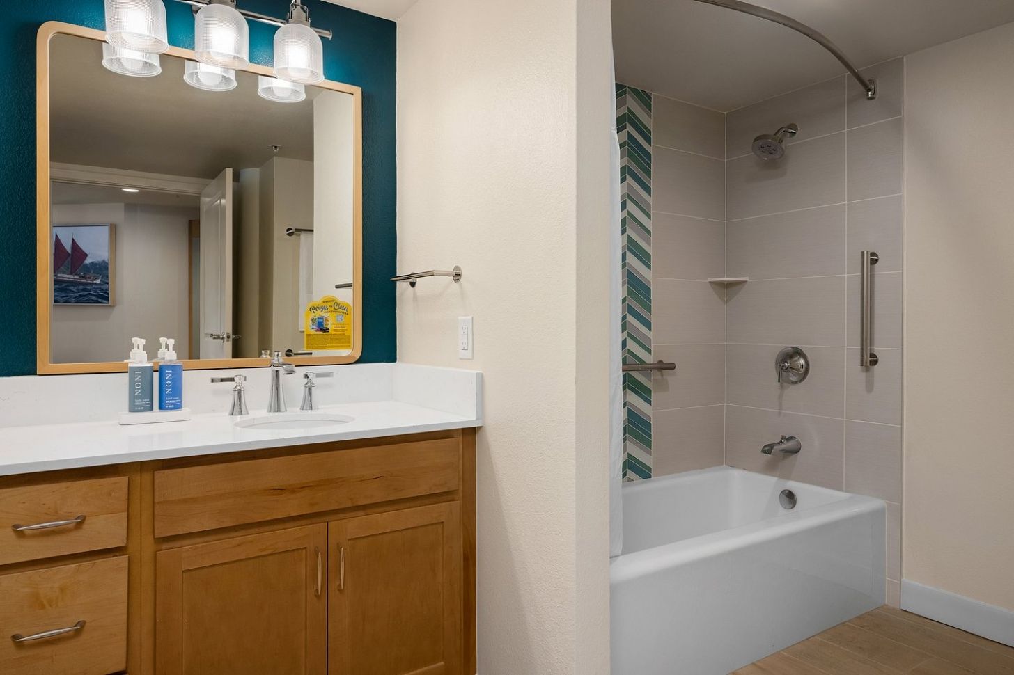 A bathroom with a white sink, wooden cabinets, a mirror with three lights, a shower with a curved door, and a striped tile wall.