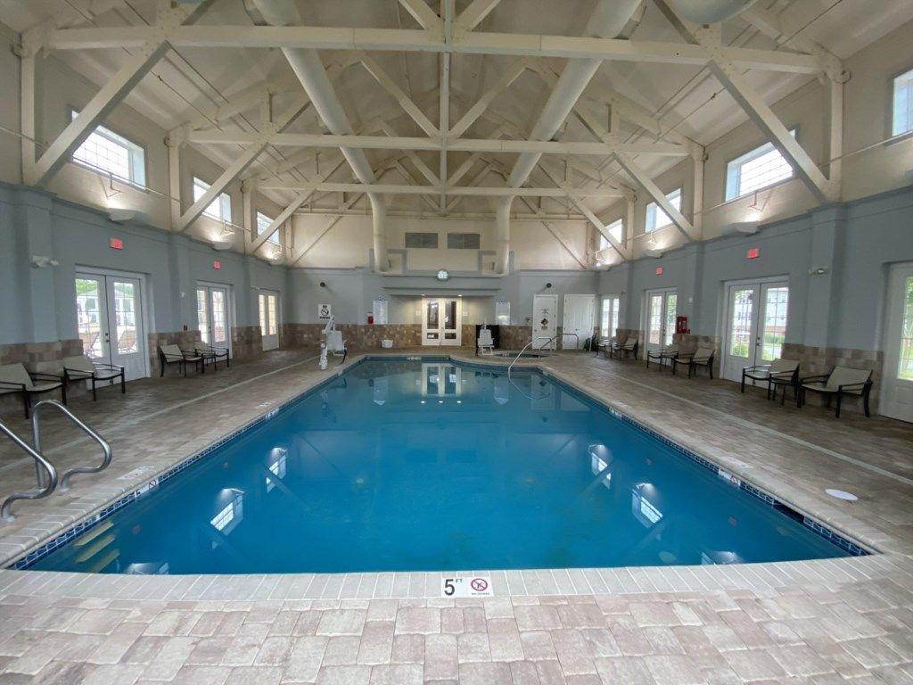 An indoor swimming pool with a high ceiling and tiled floor, surrounded by chairs and a door in the center.