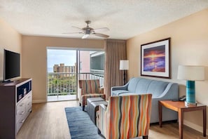 Ein Hotelzimmer mit Balkon, einer Couch, einem Fernseher und einem Gemälde.