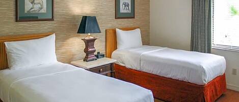 A hotel room with two beds, a nightstand, a lamp, and framed pictures on the wall.