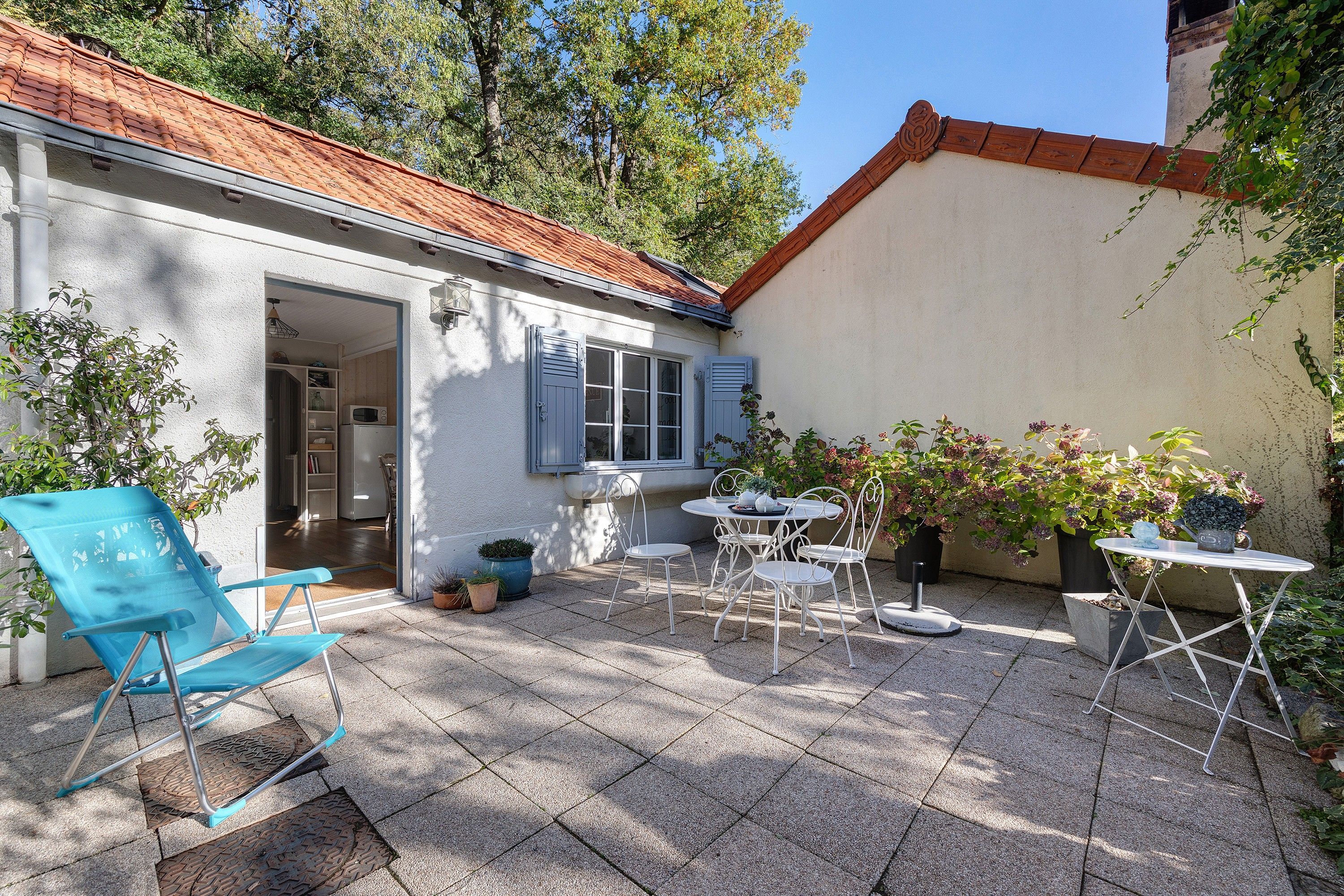 A patio area with a white building, a blue chair, a table with chairs, and potted plants.