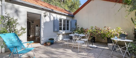 Un patio con un edificio blanco, una silla azul, una mesa con sillas y plantas en macetas.