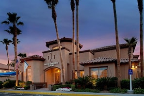 A resort building with a sign reading 'Desert Paradise Resort,' surrounded by palm trees and a clear sky. - Las Vegas | Friends Vegas Trip | Pool + Hot Tub | 2BR (Las Vegas)