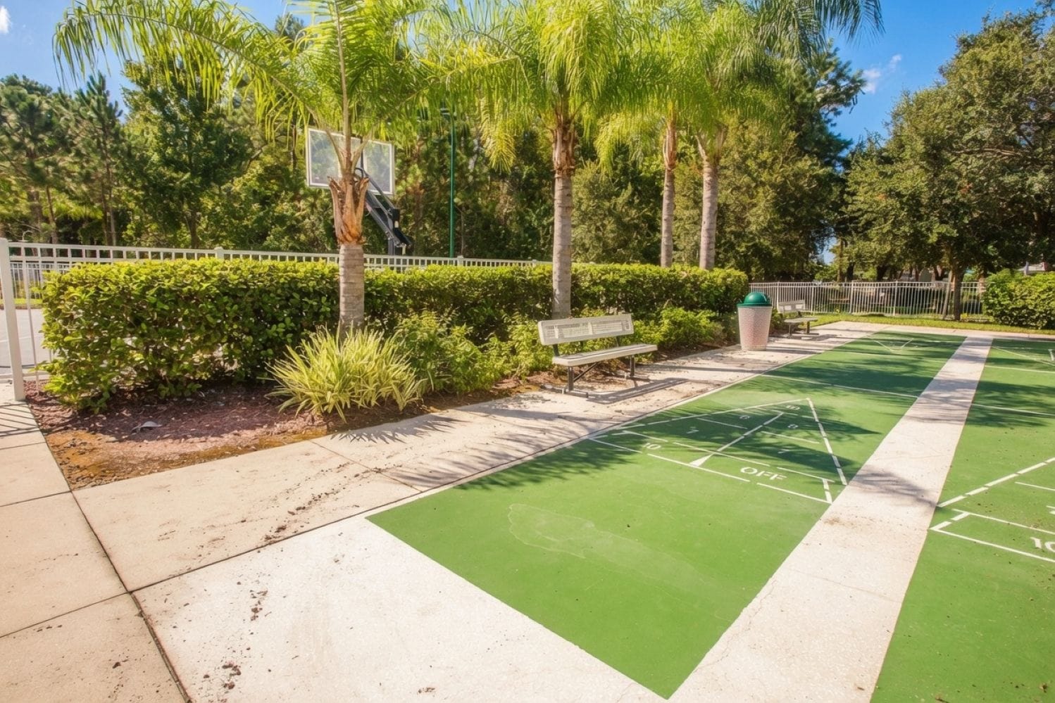 Un terrain extérieur vert avec un panier de basketball, un banc et une poubelle.