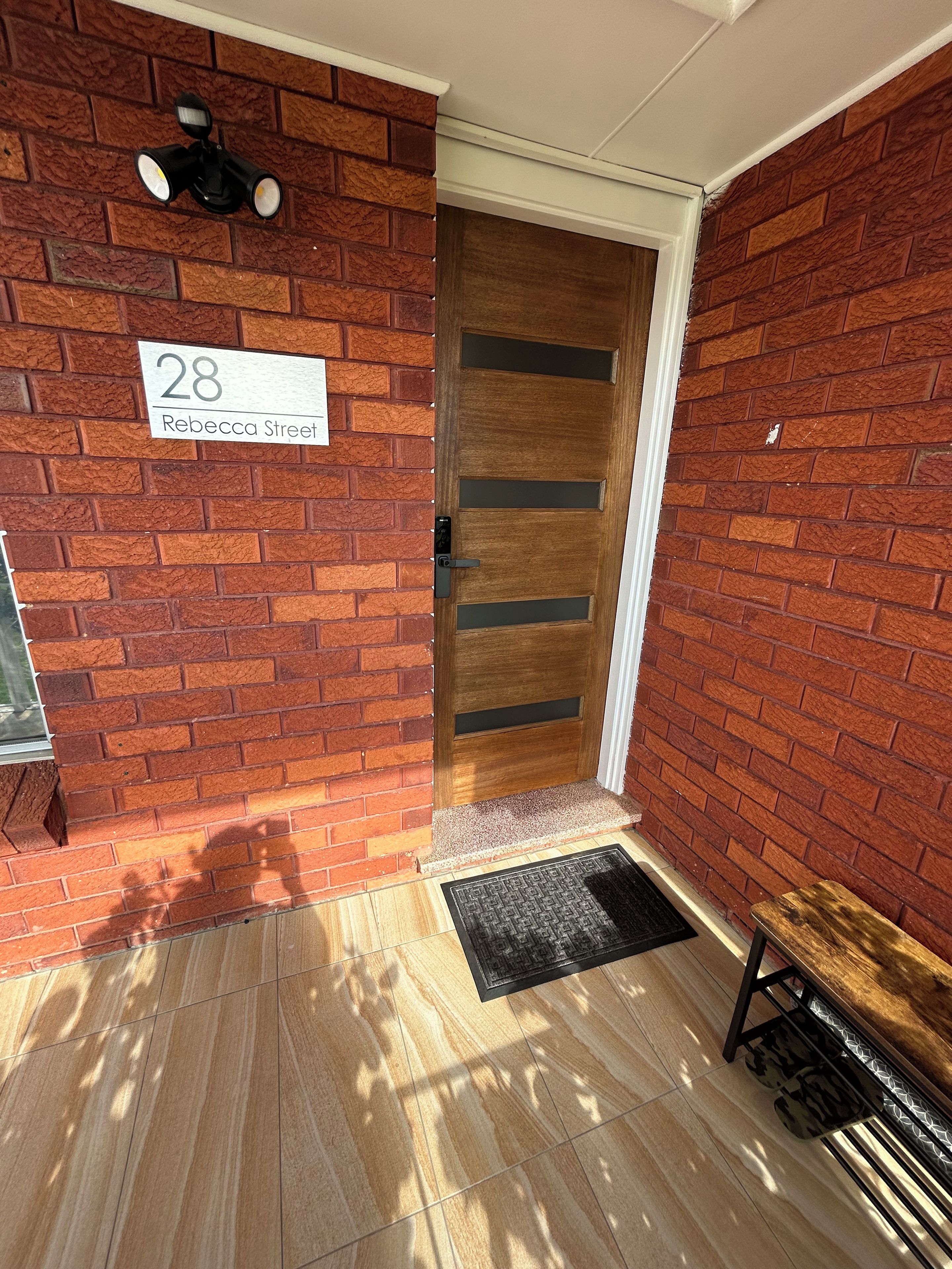 A brick exterior with a wooden door, a number sign, and a bench.