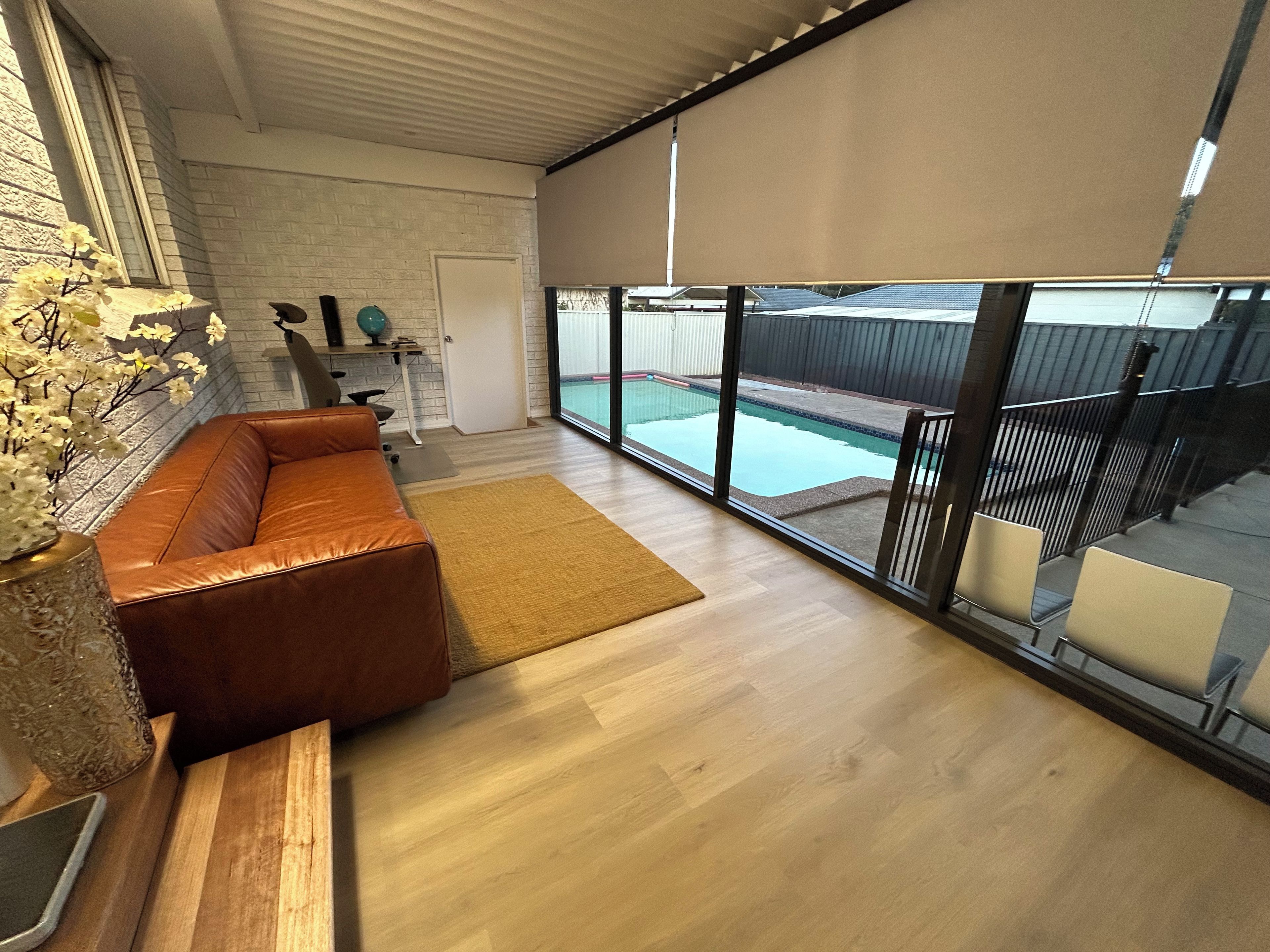A modern living room with a leather sofa, a wooden coffee table, and a large window overlooking a swimming pool.