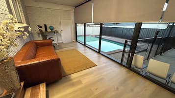 A modern living room with a leather sofa, a wooden coffee table, and a large window overlooking a swimming pool.