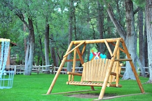 Un conjunto de columpios de madera en un parque con césped verde y árboles.