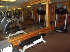 Un gimnasio con equipo de ejercicio, incluyendo cintas de correr y una banca.
