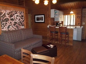 A cozy interior with a sofa, wooden chairs, a dining table, and a kitchen area with bar stools. - Payson | Peaceful Cabin Stay | Pool + Hot Tub (Payson)