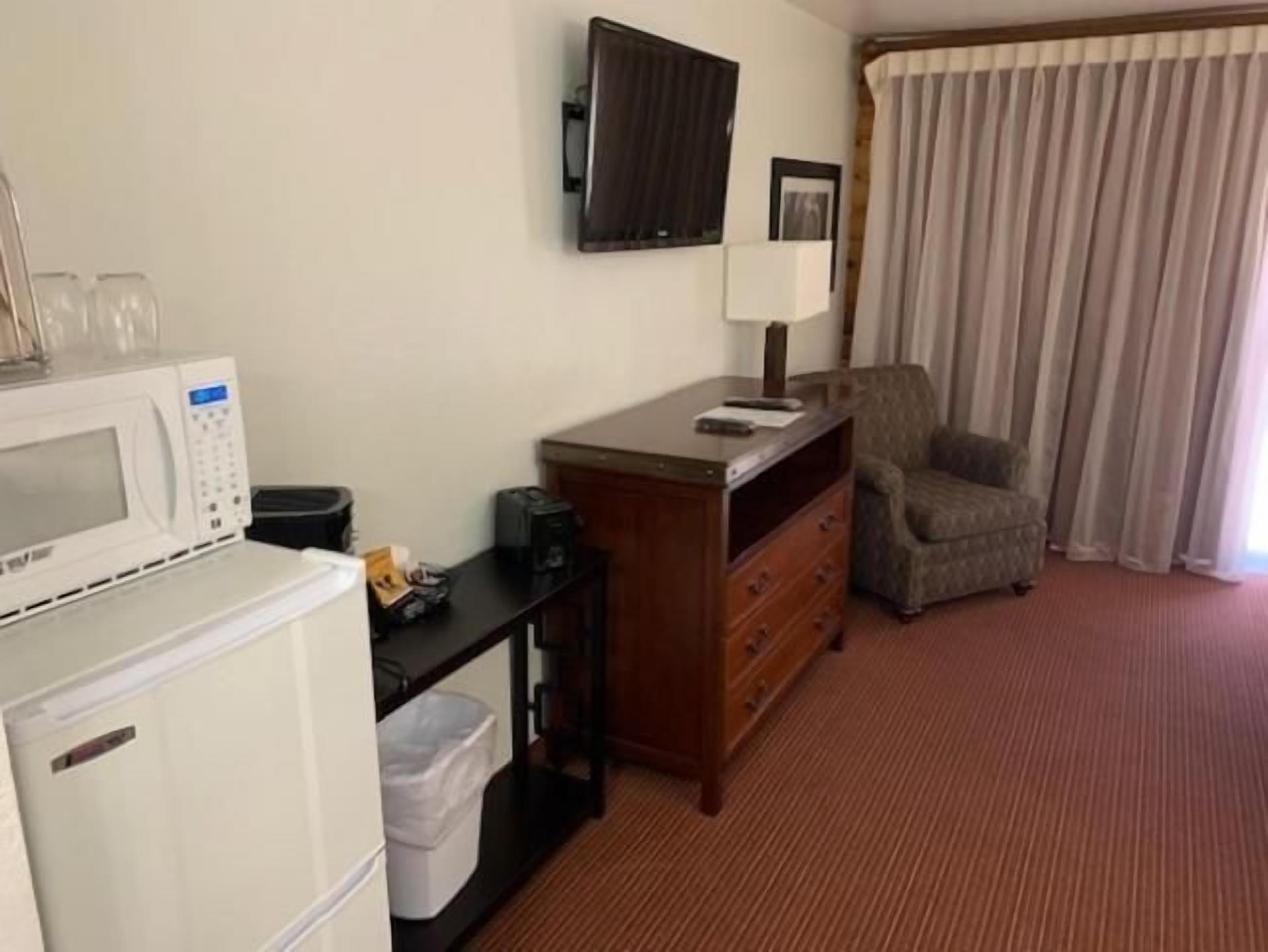 A hotel room with a kitchenette, a television, a chair, and a window with curtains.