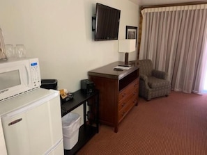 A hotel room with a kitchenette, a television, a chair, and a window with curtains. - Payson | Peaceful Cabin Stay | Pool + Hot Tub (Payson)