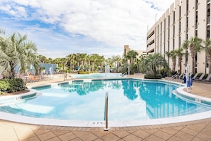 Une piscine dont la profondeur est indiquée à 3 pieds, entourée de palmiers et de chaises longues, avec un bâtiment visible à l’arrière-plan.