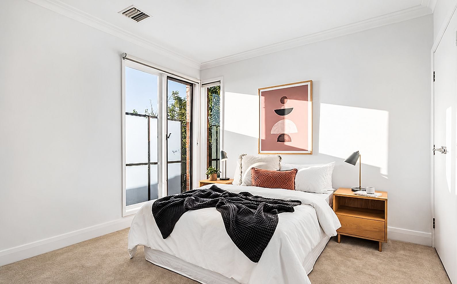 A bedroom with a bed, bedside table, lamp, and a large window with a view.