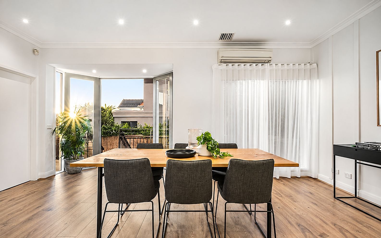 A modern dining area with a wooden table, four chairs, and a potted plant.