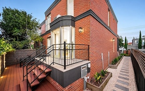 A two-story house with a balcony, a staircase leading to the entrance, and a garden area with plants. - Brighton Coastal Townhouse with 2 Private Parking (Brighton)