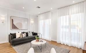 A modern living room with a grey sofa, a coffee table, and a large window with sheer curtains. - Brighton Coastal Townhouse with 2 Private Parking (Brighton)