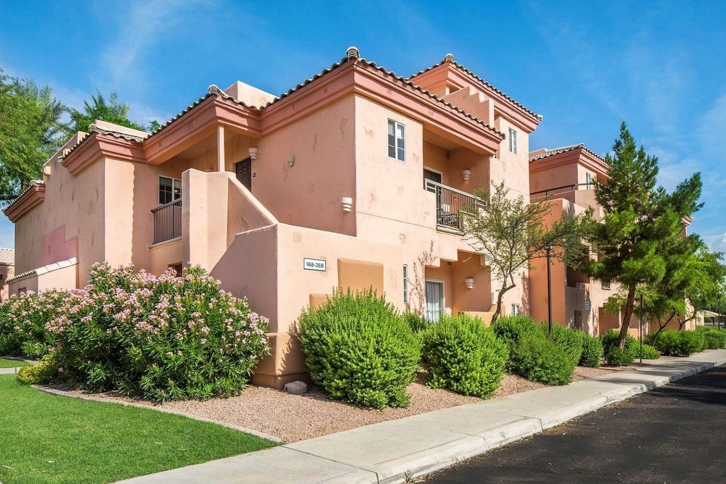 A multi-story residential building with a pink facade, balconies, and a well-maintained garden.