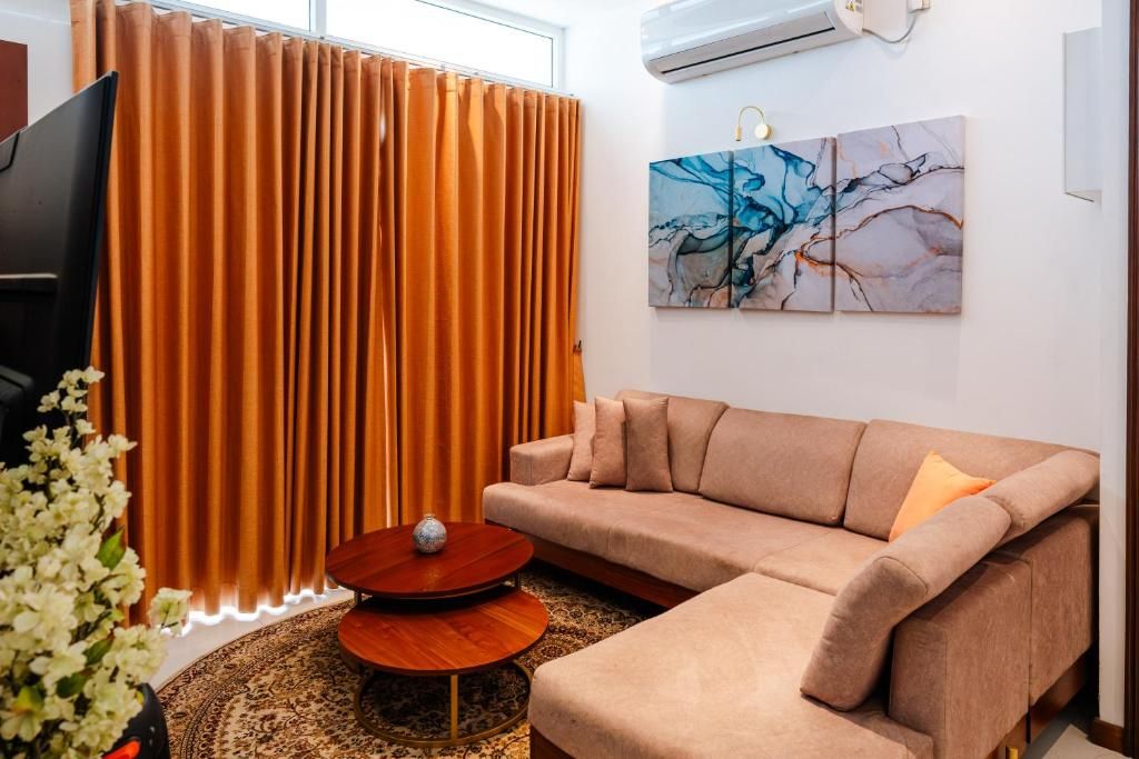A living room with a sectional sofa, a coffee table, a TV, and a large window with curtains.