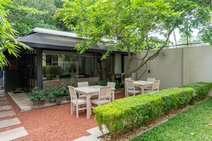 A modern outdoor seating area with tables and chairs, surrounded by greenery and a gravel path.