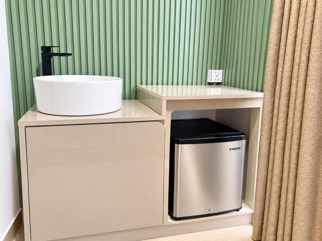 A bathroom with a white sink, a black faucet, a beige cabinet, and a silver trash bin labeled 'SINGER.'