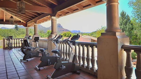 Espacio al aire libre techado con equipo de ejercicio, columnas y vistas a montañas.