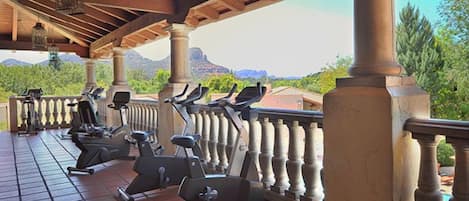Espacio al aire libre techado con equipo de ejercicio, columnas y vistas a montañas.