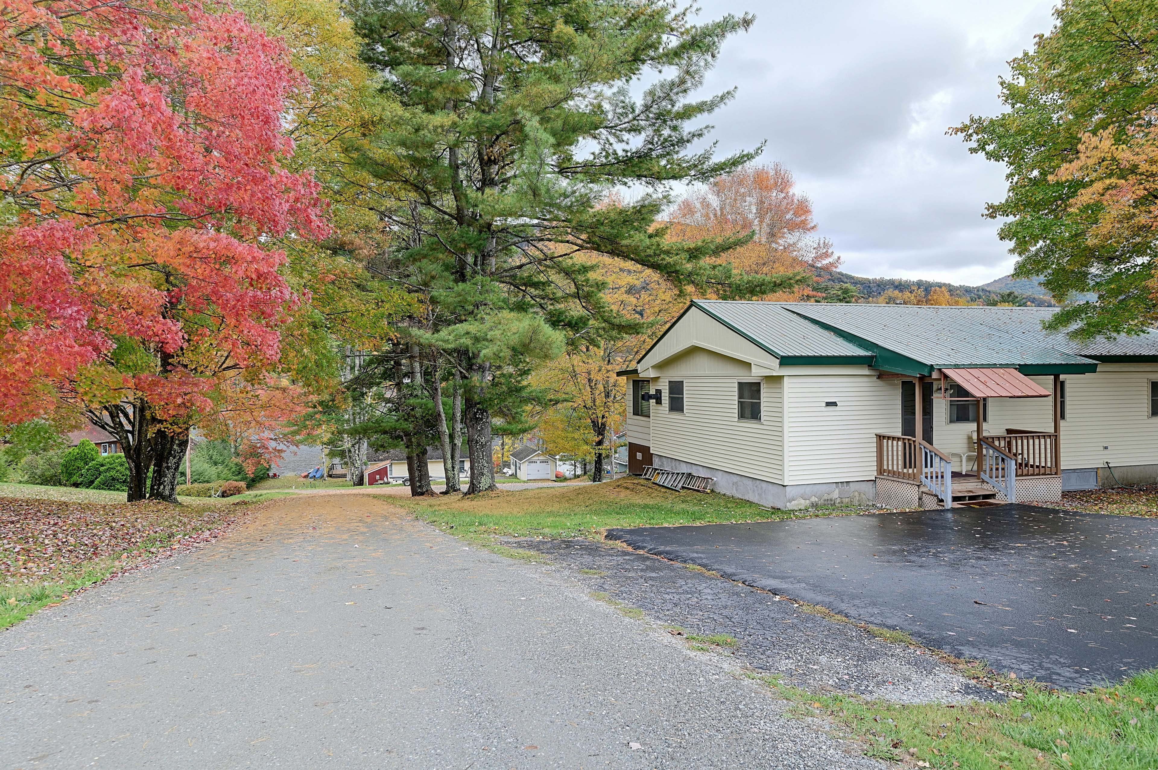 A single-story cabin with a green roof, a front porch, and a driveway leading to the entrance.