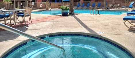 Un área de piscina con sillas de descanso, un jacuzzi y una zona vallada junto a la piscina.