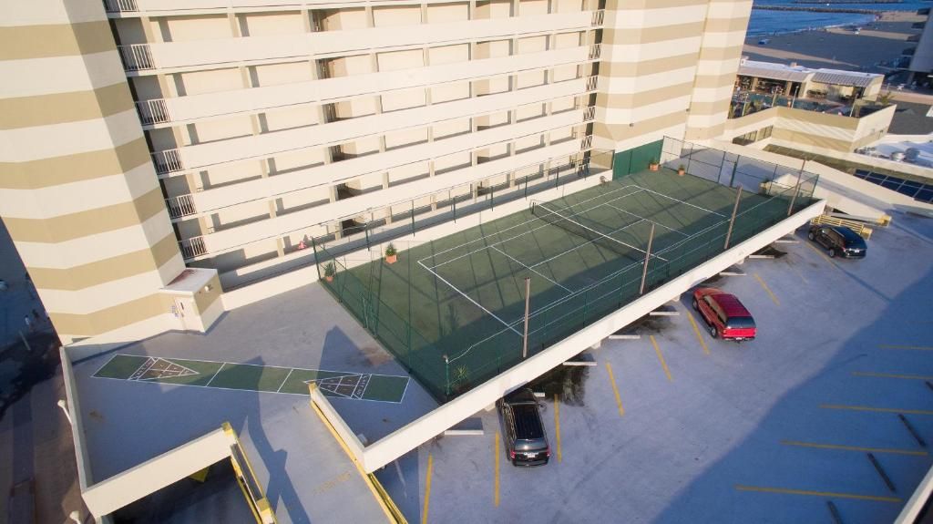 Luchtbeeld van een hotel met een tennisbaan, meerdere parkeerplaatsen en een gebouw met balkons.